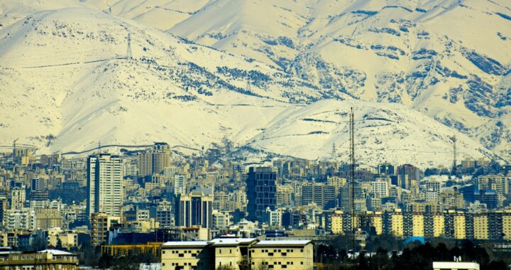 Foto mostrando montanhas nevadas ao fundo de uma cidade com prédios altos.