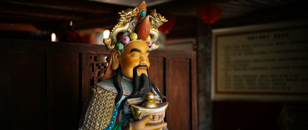 Foto de estátua da deidade taoísta chinesa que atrai fortunas – um homem de cavanhaque, com trajes coloridos, portando um lingote de ouro.