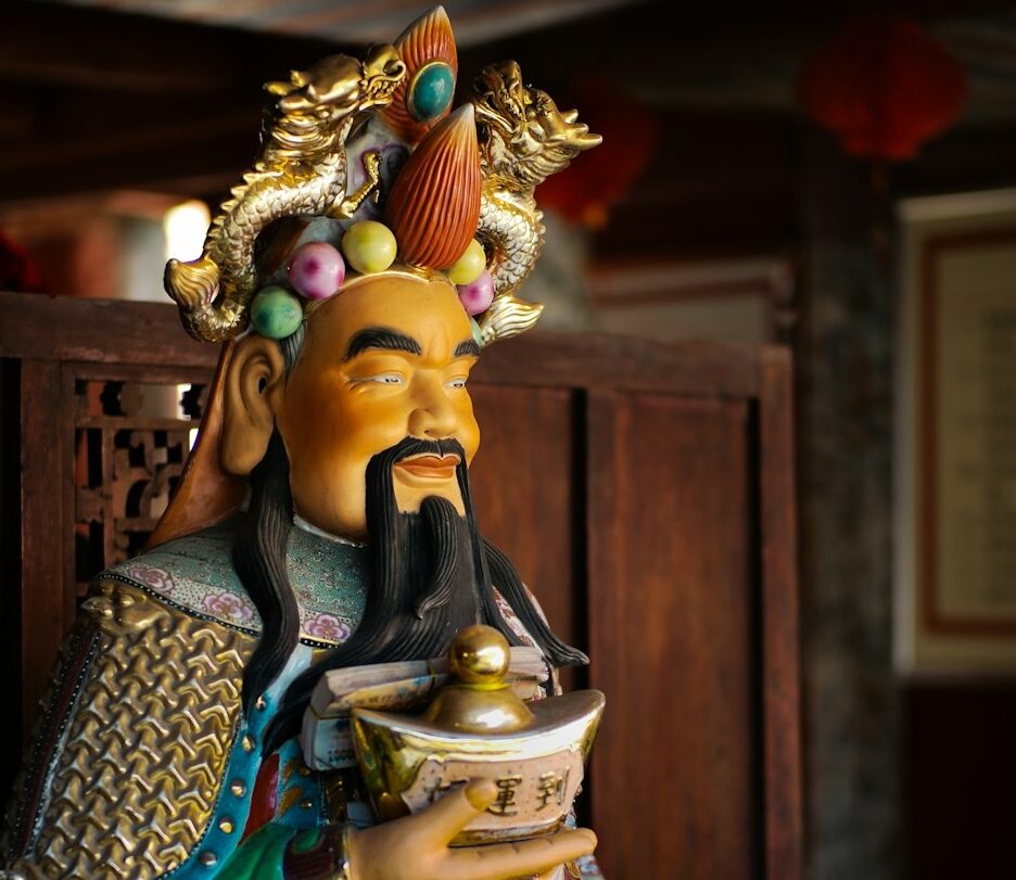 Foto de estátua da deidade taoísta chinesa que atrai fortunas – um homem de cavanhaque, com trajes coloridos, portando um lingote de ouro.