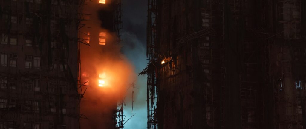 Foto noturna em cores de foco de incêndio em prédio cercado de andaimes.