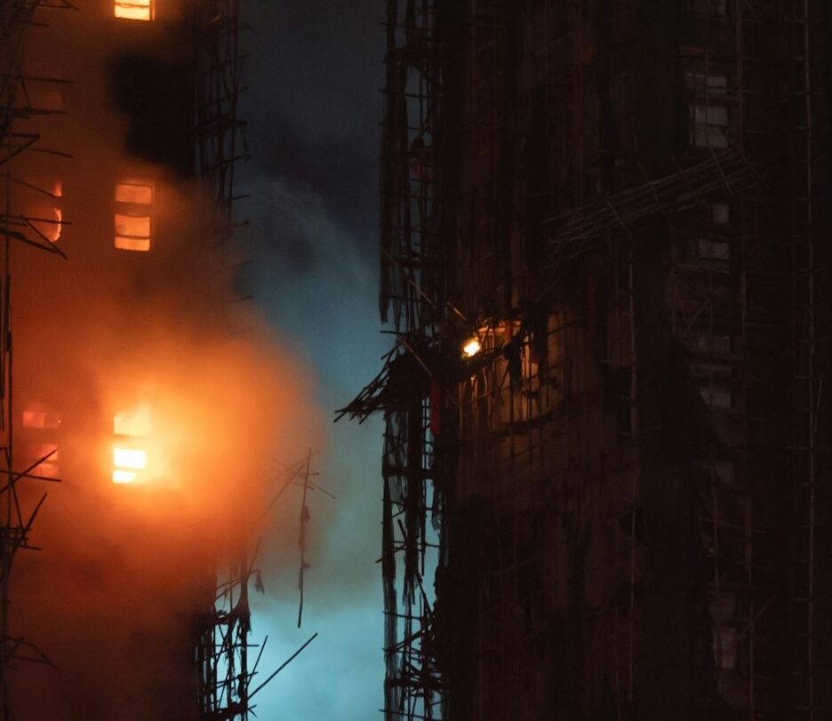 Foto noturna em cores de foco de incêndio em prédio cercado de andaimes.