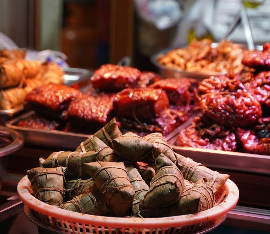 Fotografia em cores de diversas carnes em variados preparos ao estilo chinês expostas em balcão de loja.