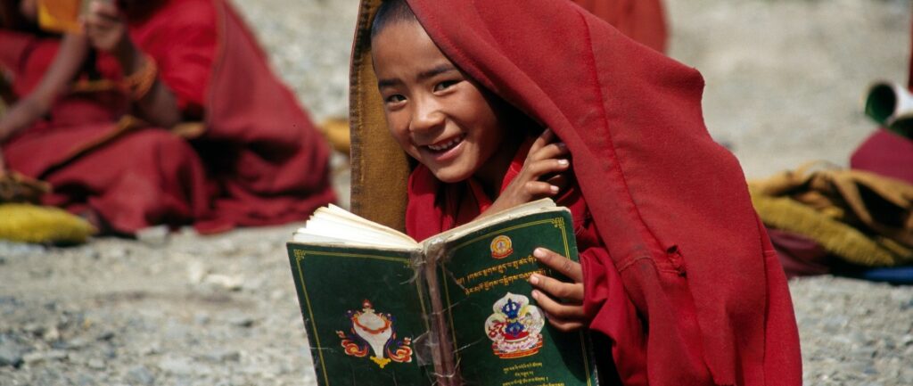 Fotografia em cores de criança tibetana lendo um livro que não está escrito em mandarim.