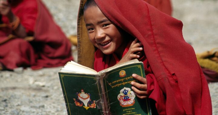 Fotografia em cores de criança tibetana lendo um livro que não está escrito em mandarim.