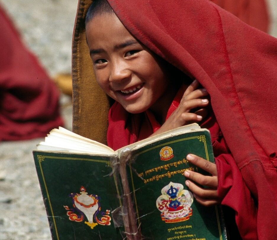 Fotografia em cores de criança tibetana lendo um livro que não está escrito em mandarim.