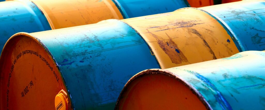 Foto em cores de barris azuis e amarelos de petróleo.
