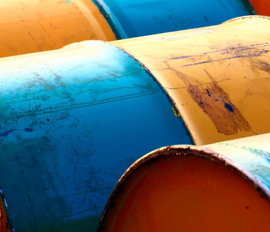 Foto em cores de barris azuis e amarelos de petróleo.