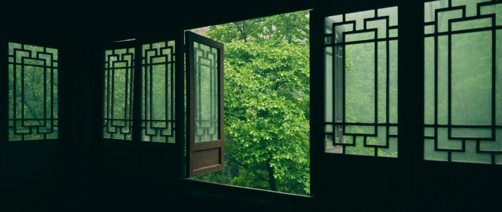 Foto em cores de copas de árvores vistas a partir de janela de estética tradicional chinesa.