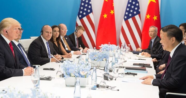 mesa de reunião com Trump e equipe sentados de um lado e do outro Xi Jinping e equipe, com bandeiras no fundo